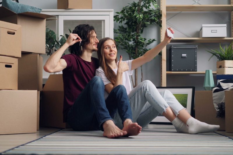 Home 9 Young couple sitting among moving boxes taking a selfie cele 1791306358